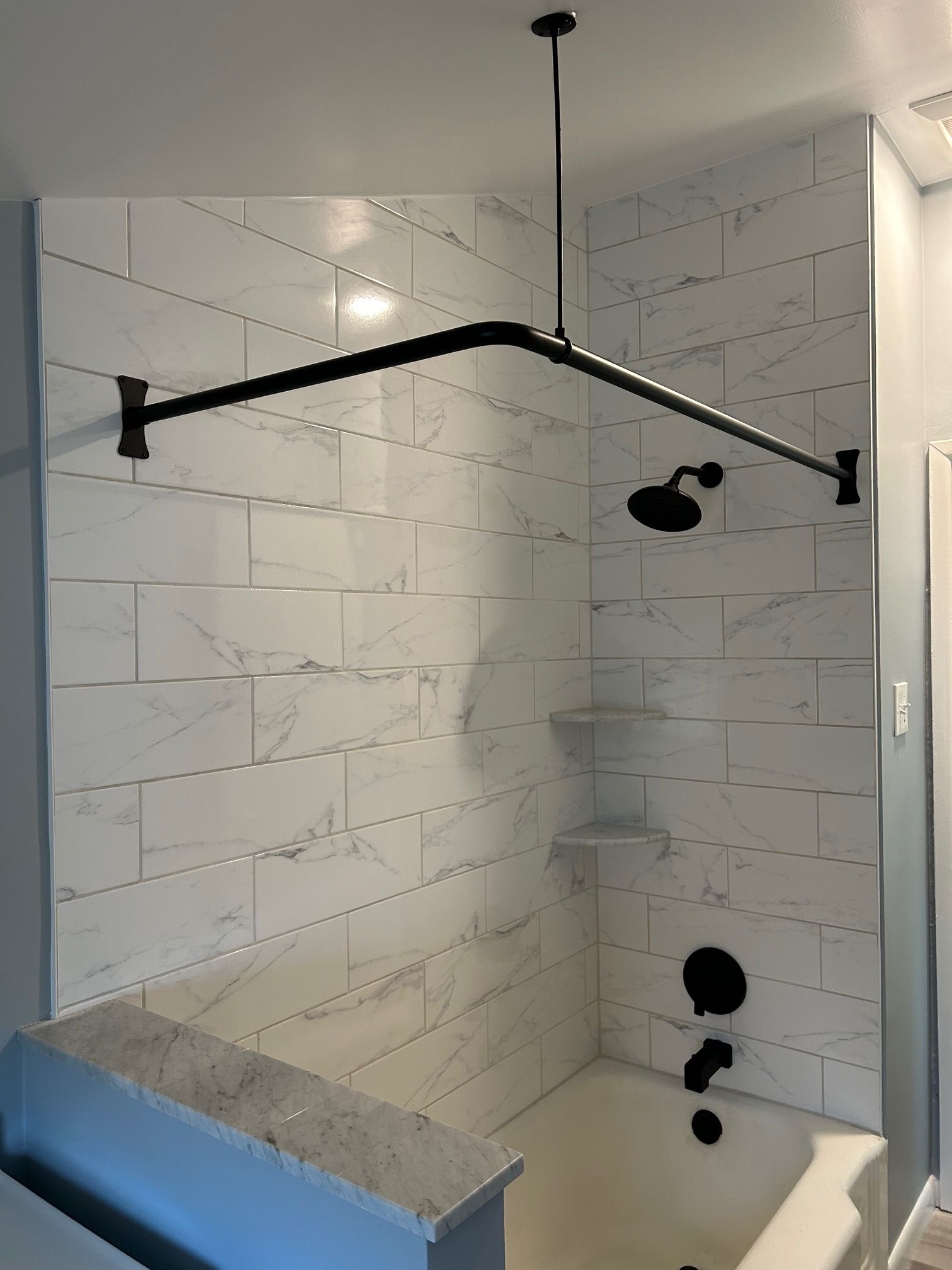 Walk-in shower with white tile walls, black fixtures, and a handheld showerhead
