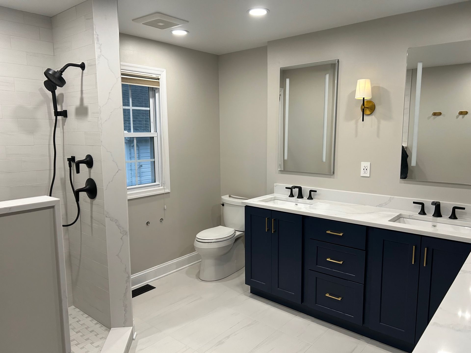Modern bathroom with white shower, navy vanity, mirrors, and toilet on light tile floor