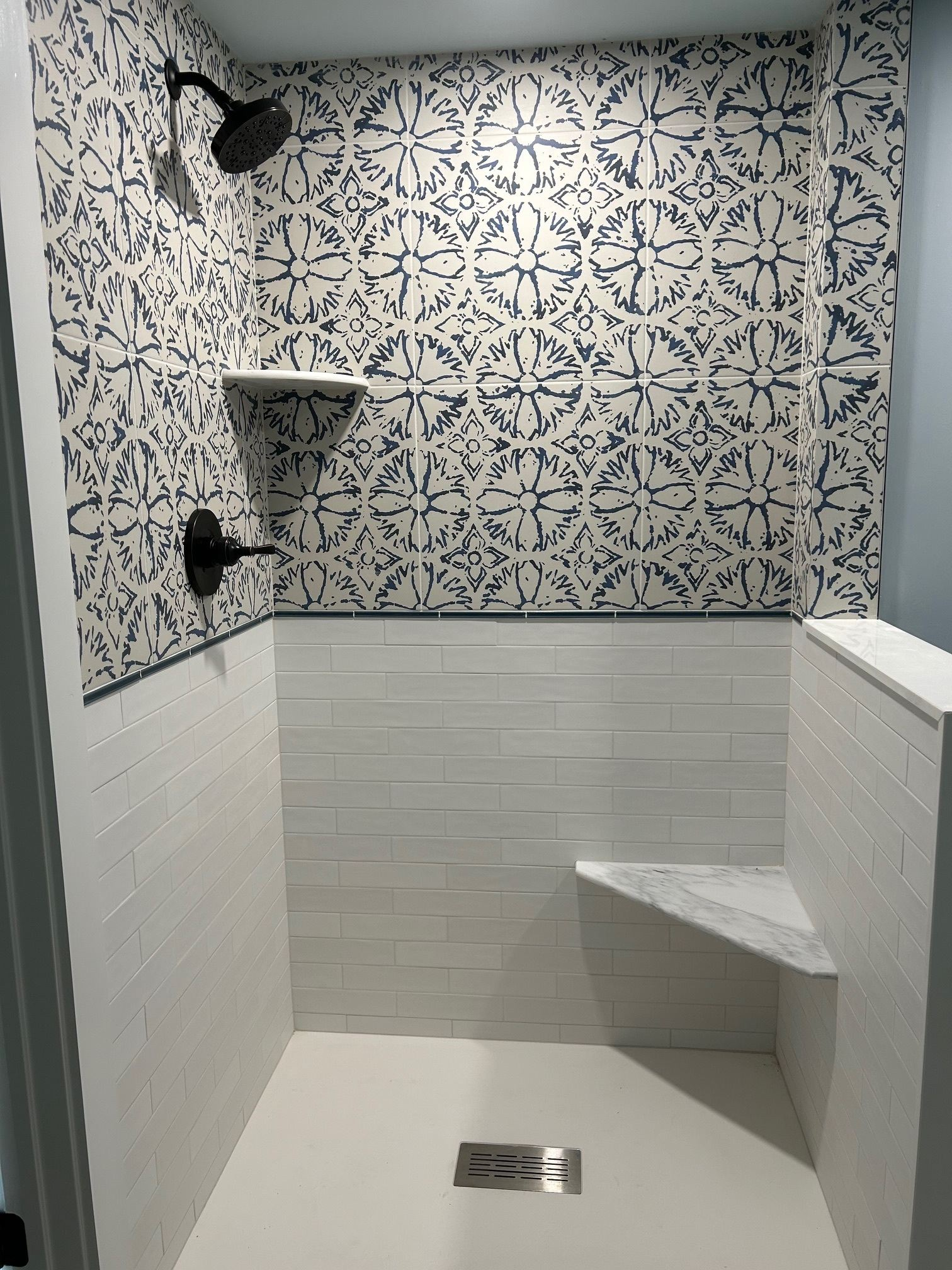 Small tiled shower stall with patterned upper walls, built-in bench, and black fixtures.