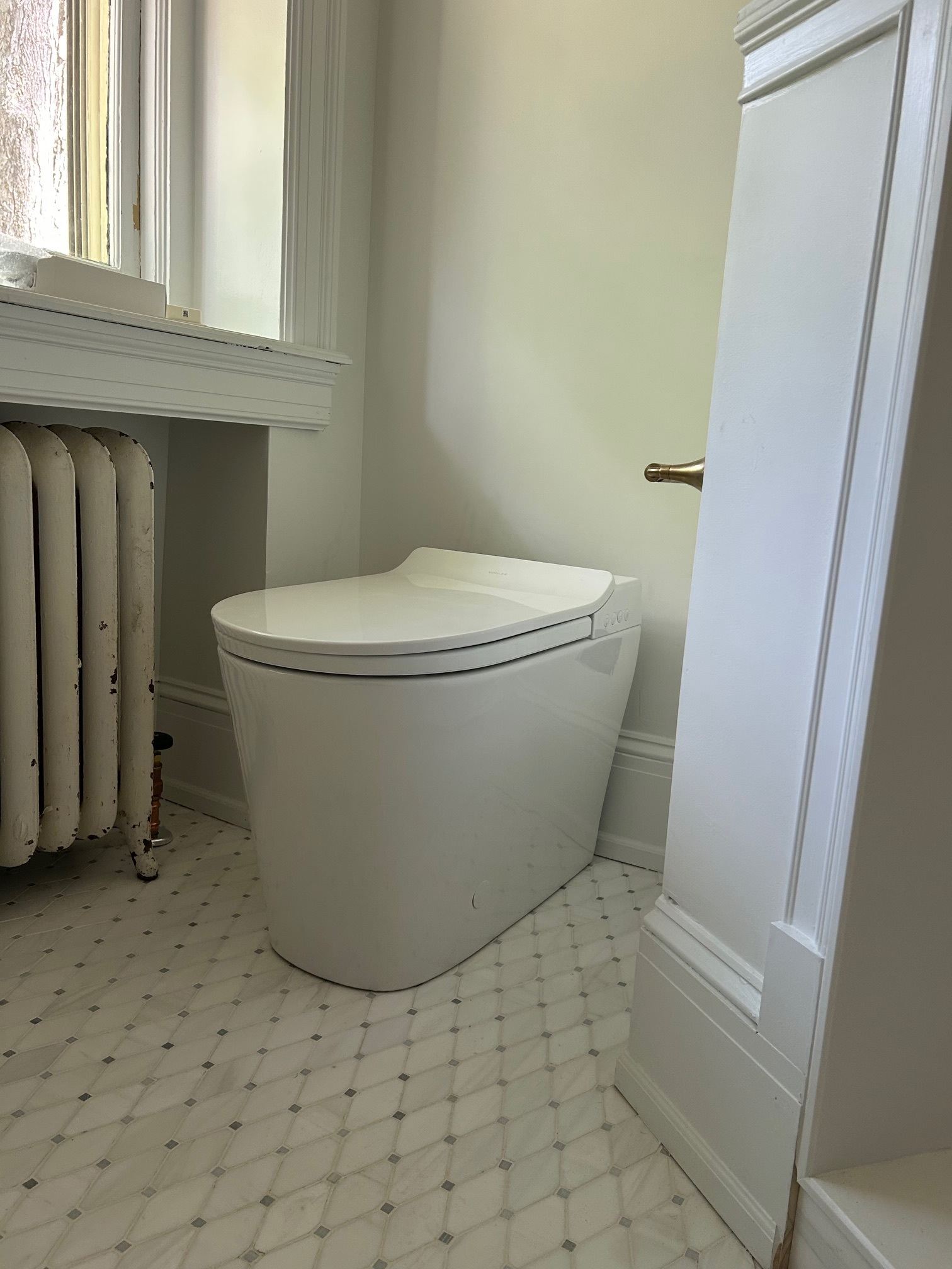 Small bathroom with a compact white toilet beside a window and radiator, viewed from the doorway.