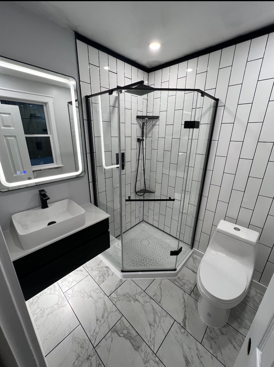 Modern black-and-white bathroom with glass shower, vanity sink, and toilet.