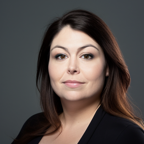 A woman with long brown hair is wearing a black shirt and looking at the camera.