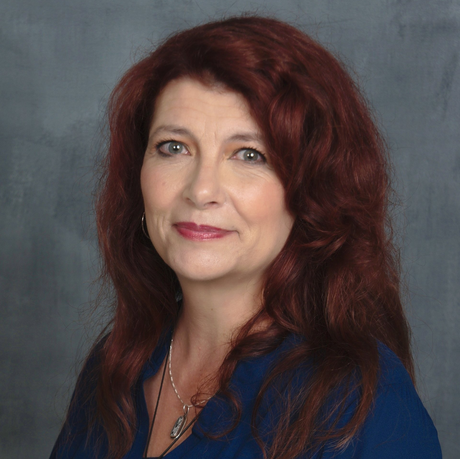 A woman with red hair is wearing a blue shirt and a necklace.