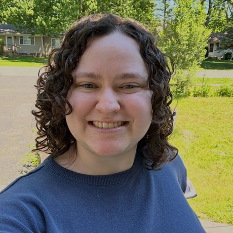 A woman with curly hair is smiling and wearing a green shirt.