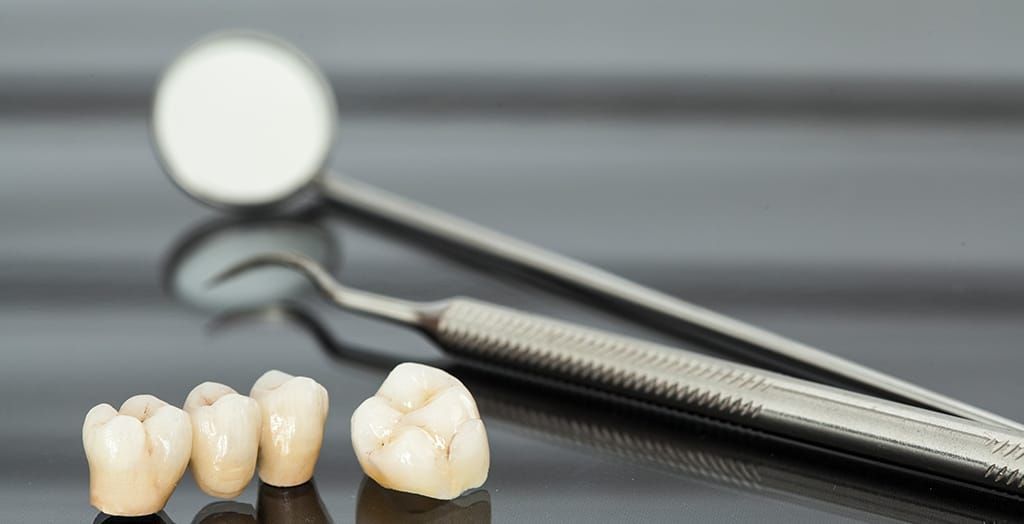Three dental crowns and a dental mirror on a table. Three dental crowns and a dental mirror on a table.