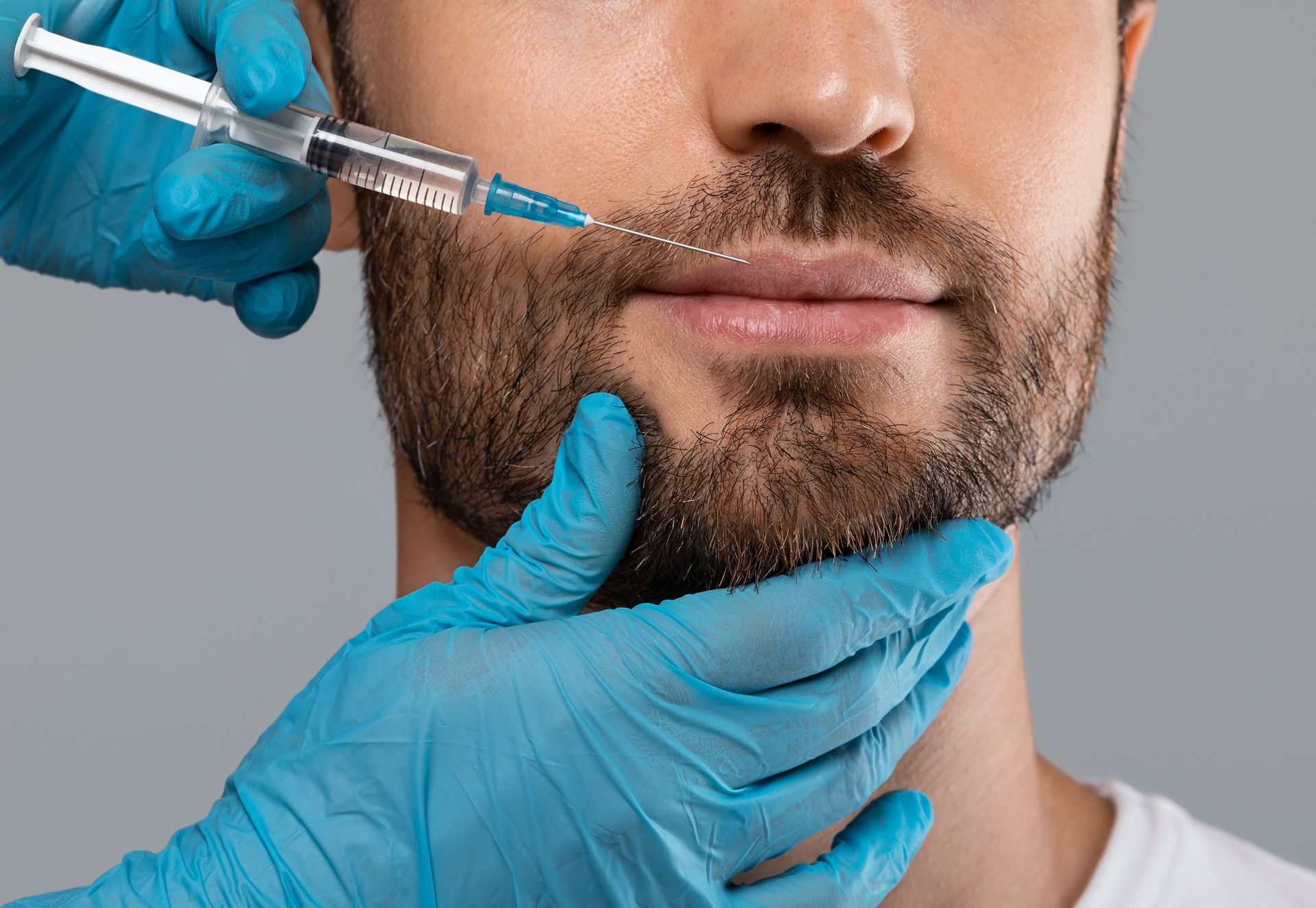 A man with a beard is getting a botox injection in his lips. A man with a beard is getting a botox injection in his lips.