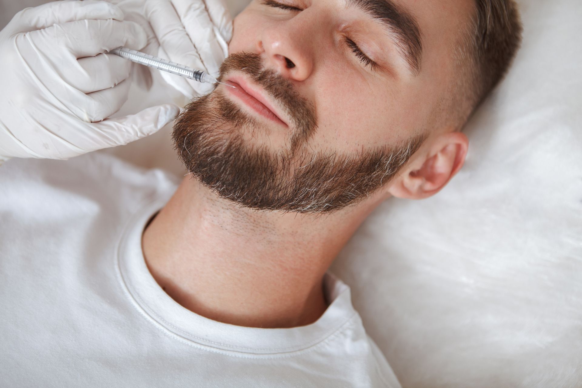 A man with a beard is getting a botox injection in his face. A man with a beard is getting a botox injection in his face.