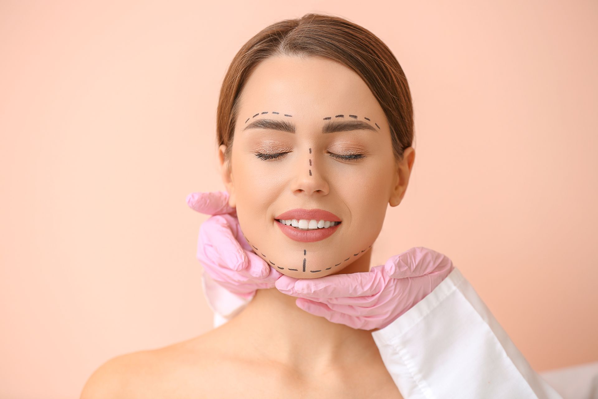 Woman receiving facial treatment with pink gloves against a peach background