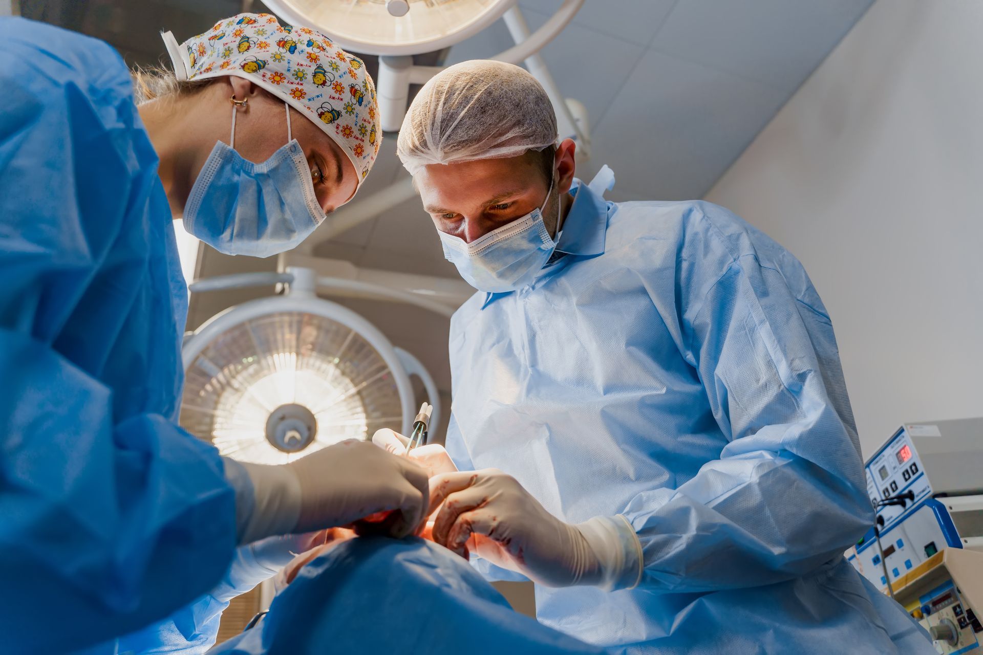 Surgeons in blue scrubs perform a procedure in an operating room under bright lights