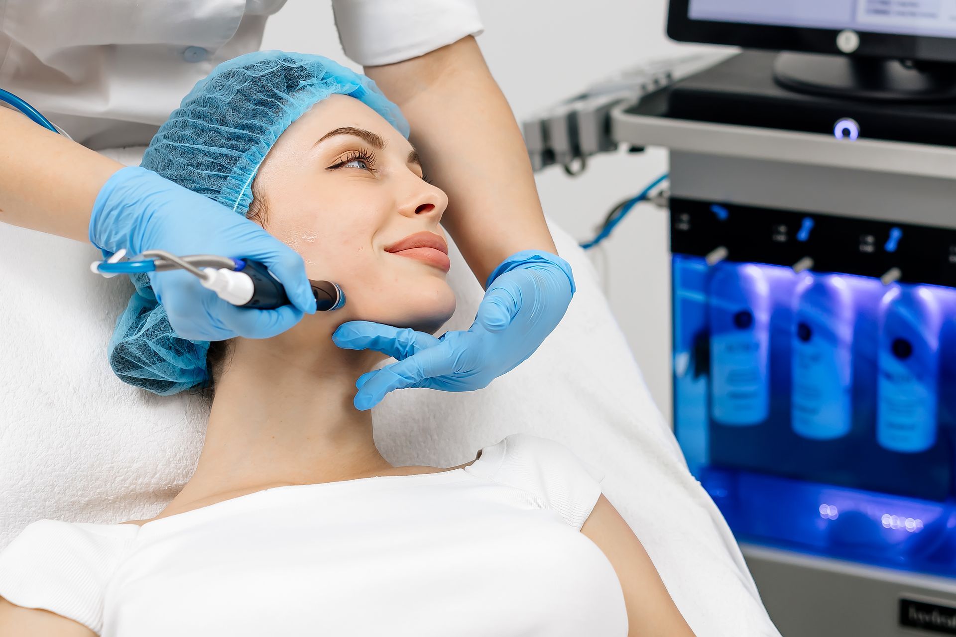 Woman receiving a facial treatment with gloved hands beside a glowing skincare machine