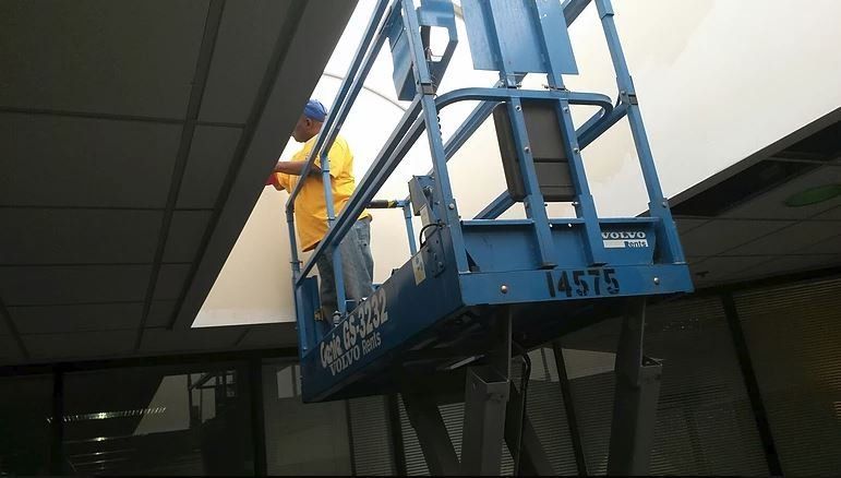 Person in a blue lift working on a ceiling panel indoors.