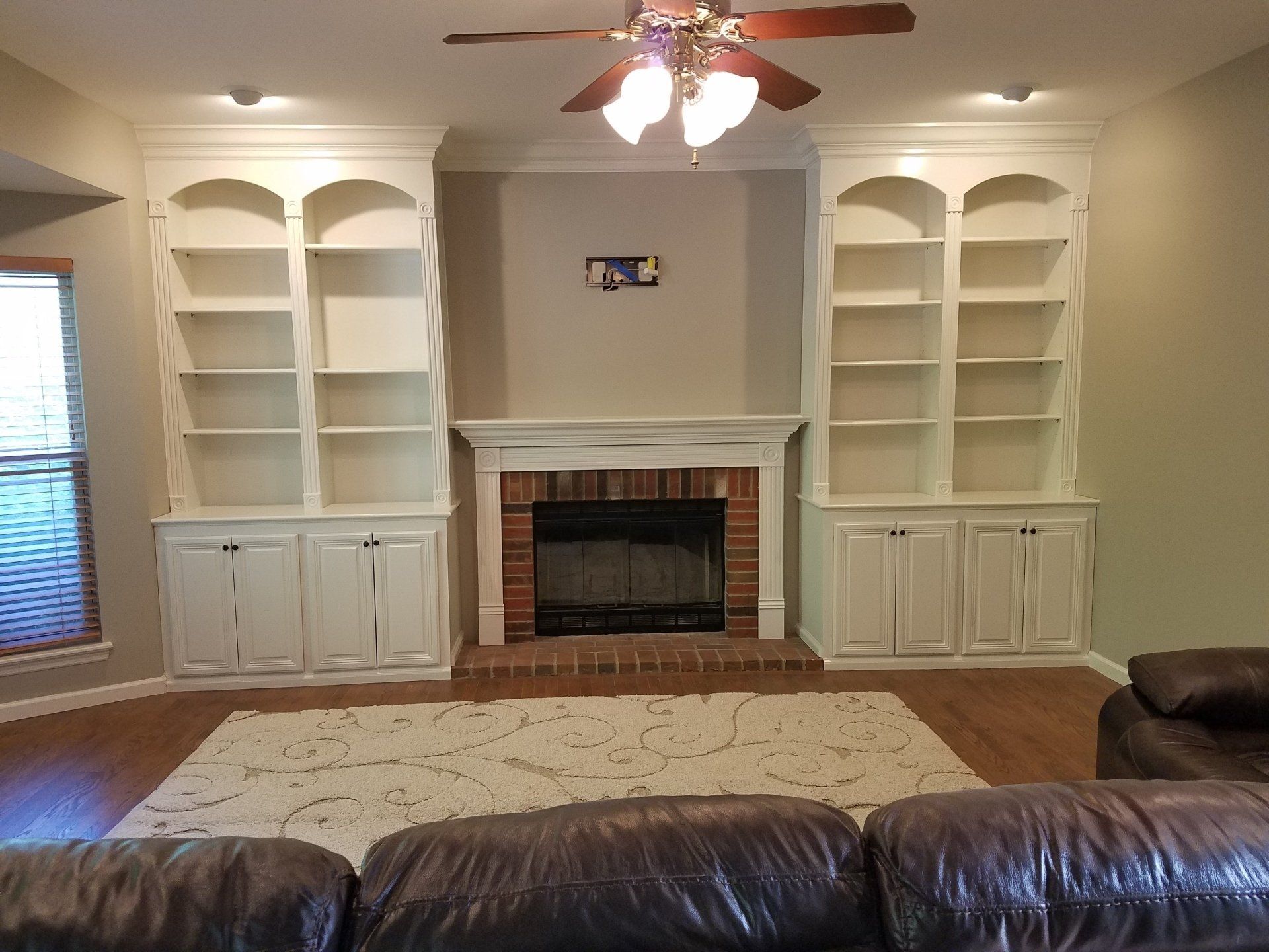 Built-in white bookshelves flank a fireplace. A brown leather couch sits in front.
