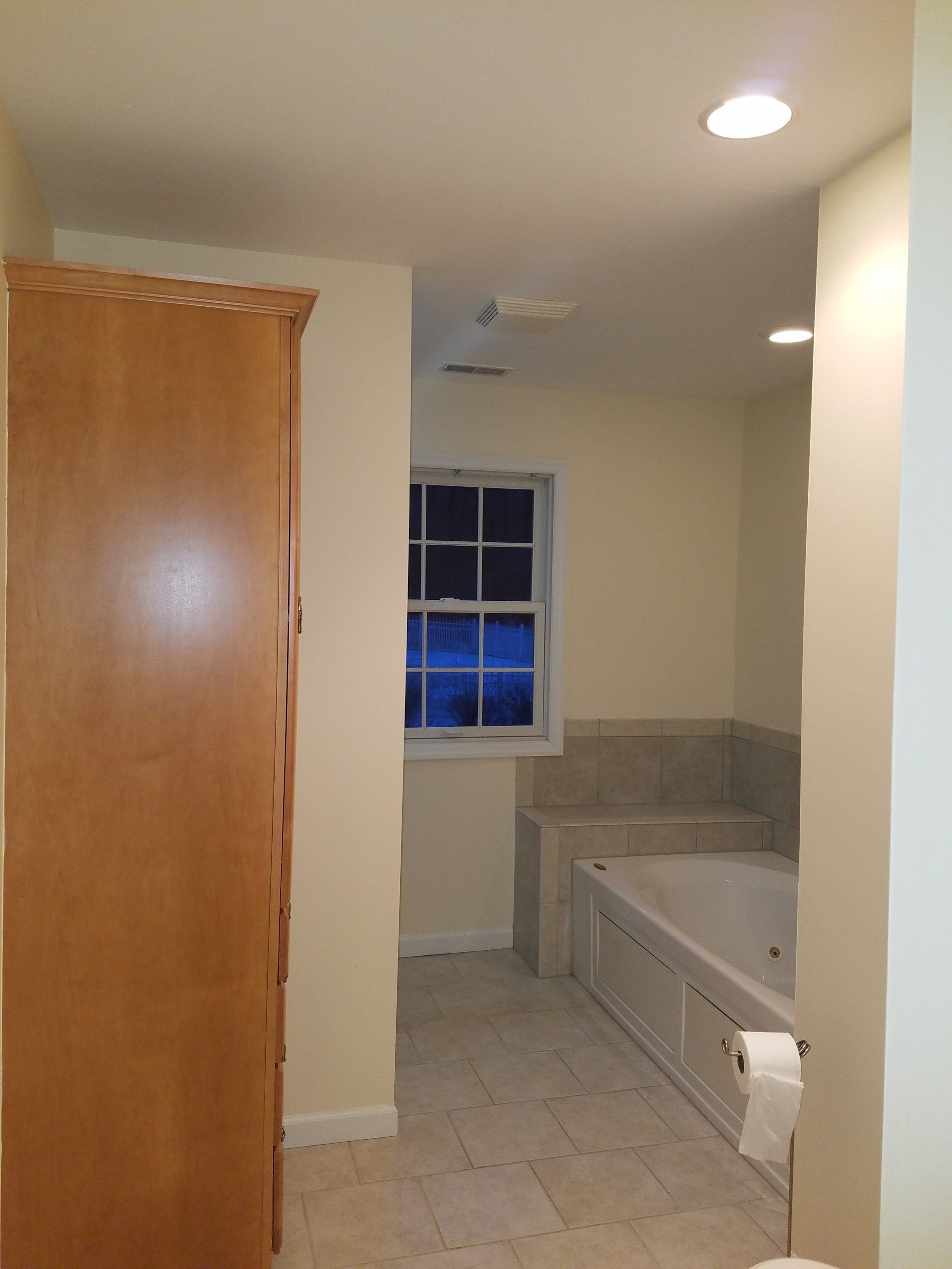 Bathroom with tall wooden cabinet, window, and built-in tub.