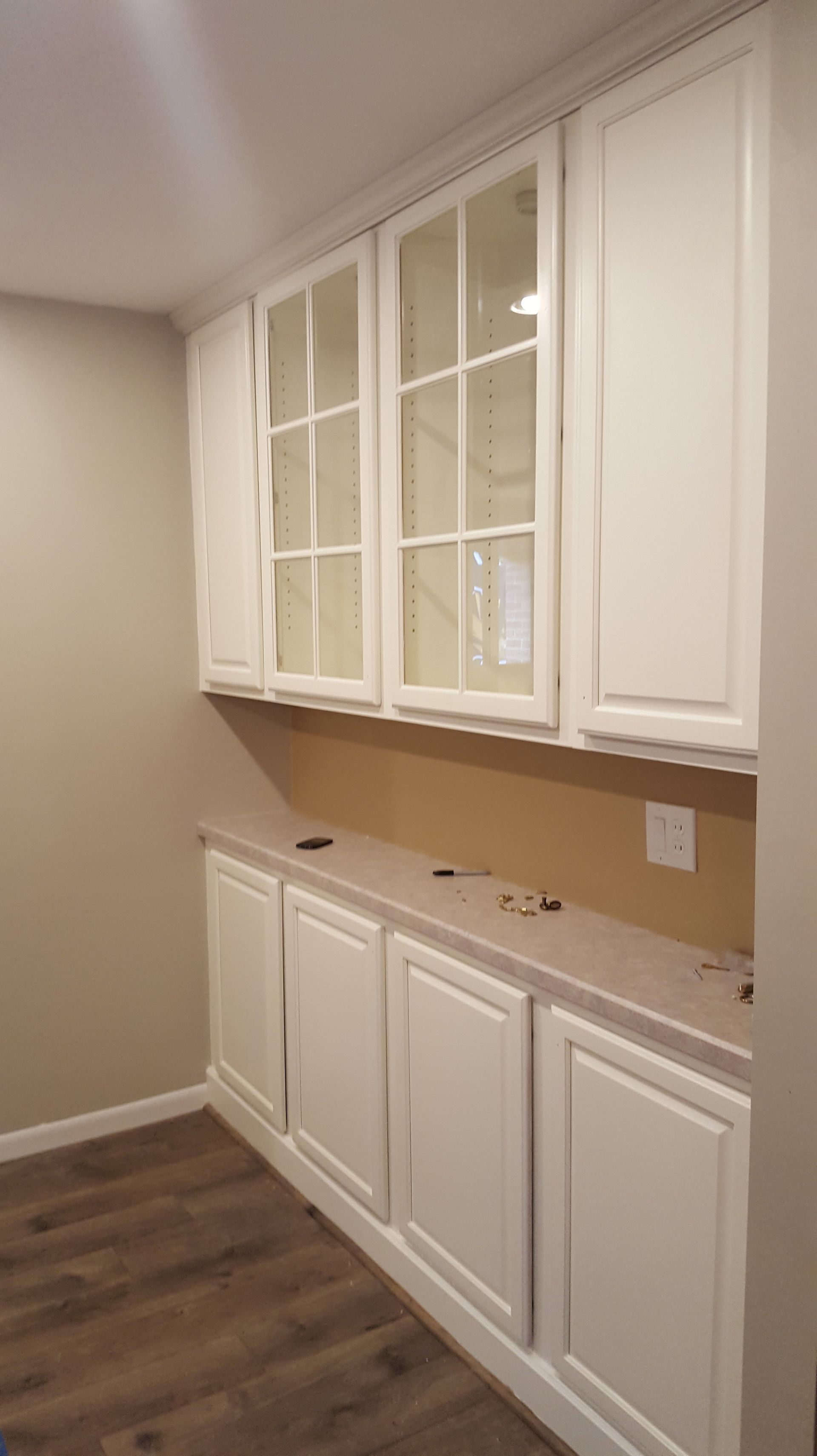 White cabinets in a kitchen. Upper cabinets have glass-paned doors. Lower cabinets sit below a countertop.