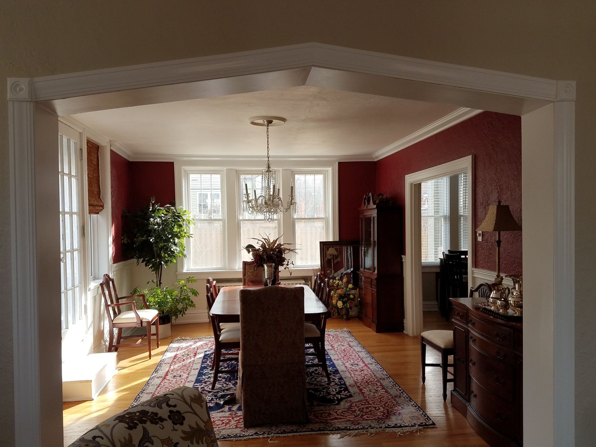 Dining room with red walls, chandelier, wooden table, and oriental rug.