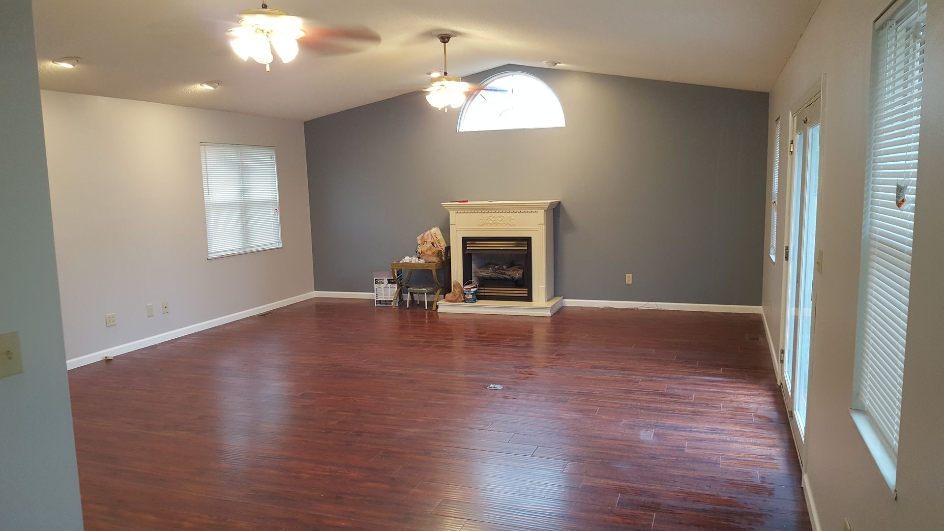 Spacious living room with wood floor, fireplace, two ceiling fans, and gray and white walls.