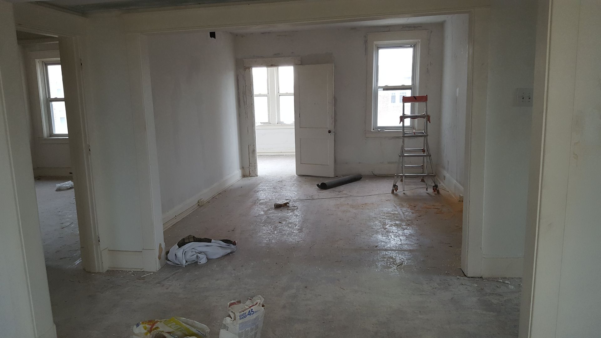 Interior room undergoing renovation with partially finished walls, floor debris, and a ladder.