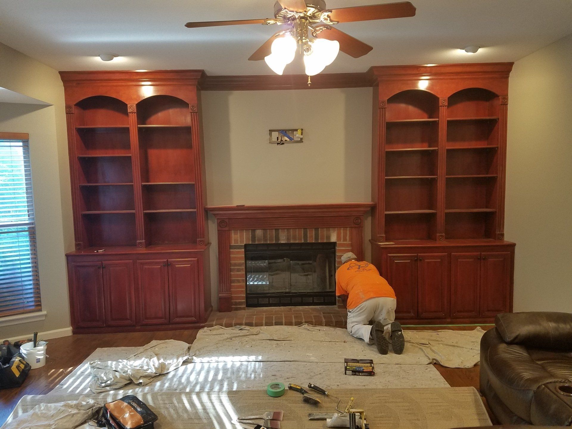 Person painting a built-in entertainment center with bookshelves and a fireplace.