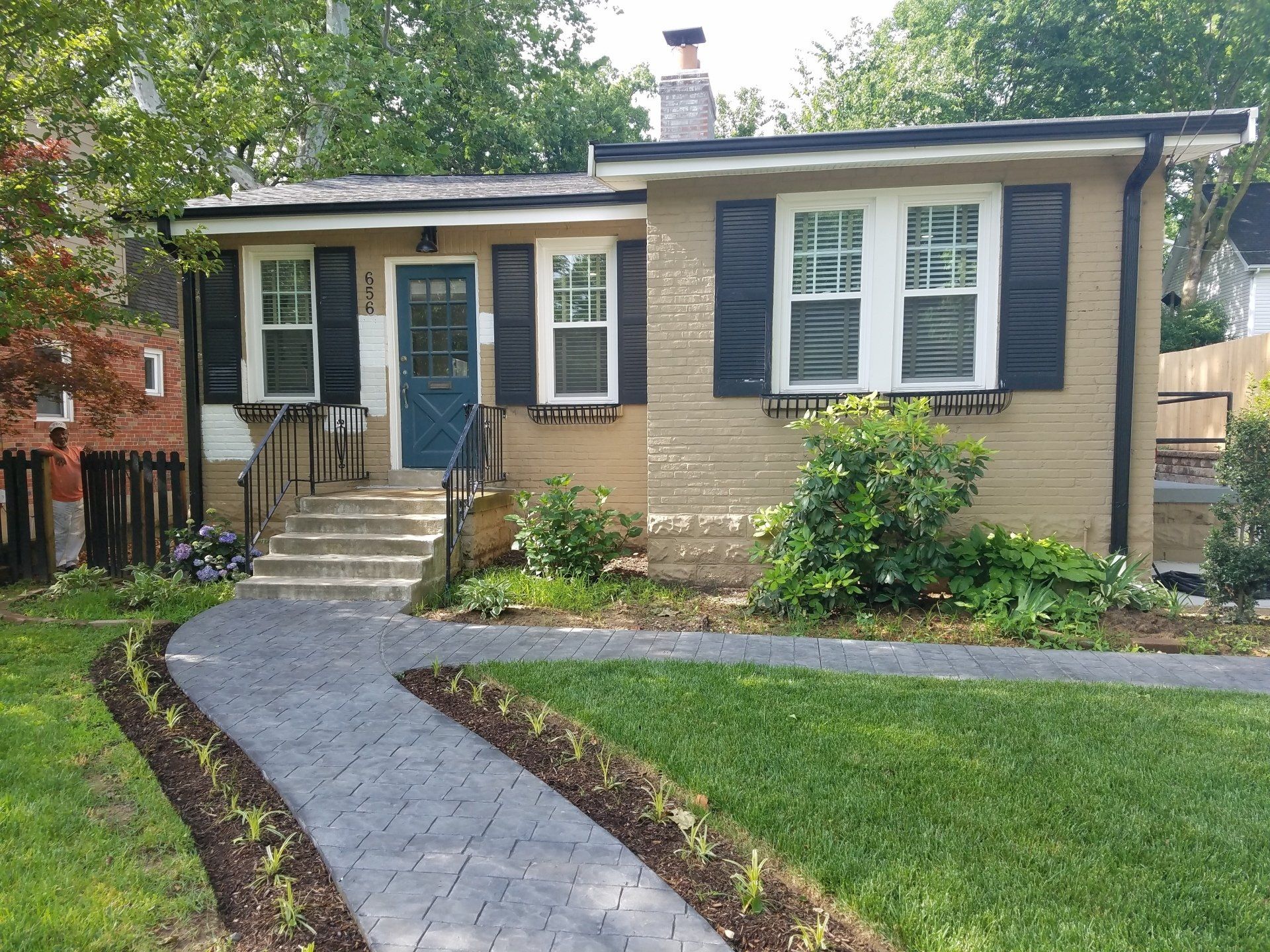 Tan bungalow with a blue door, black shutters, and a brick walkway.