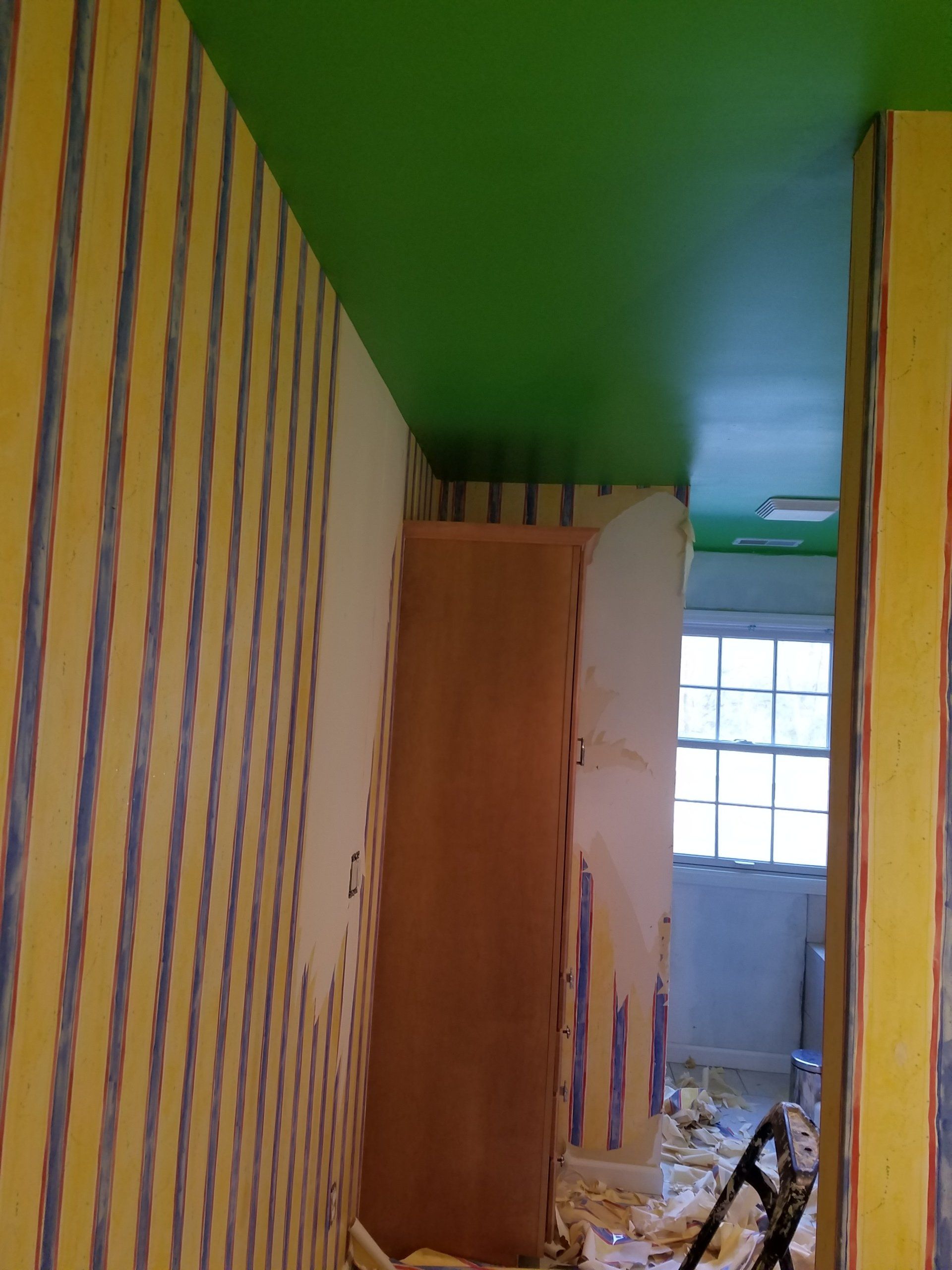 Room with striped wallpaper, green ceiling, doorway with a window, and a wooden cabinet.