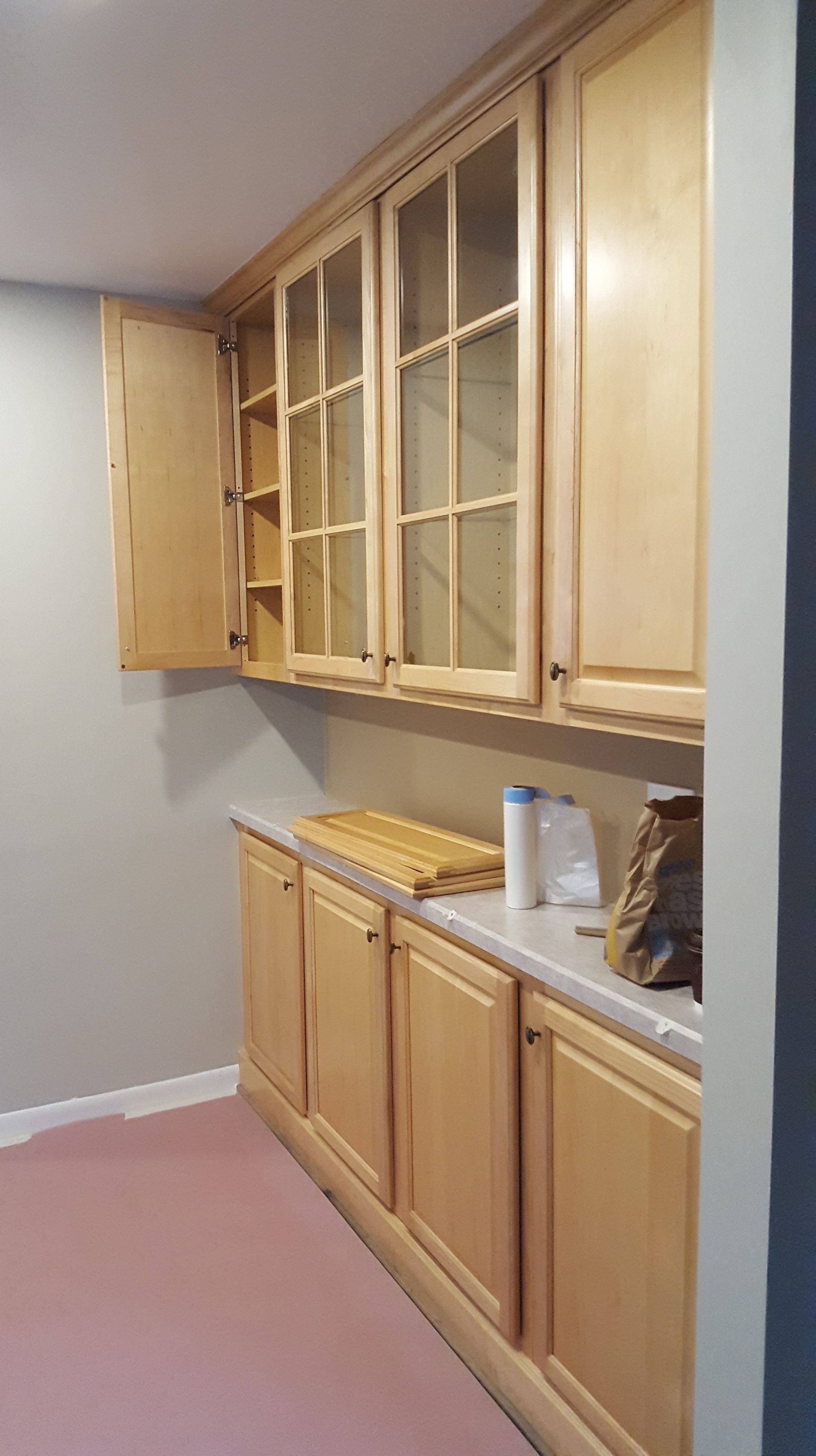 Light wood cabinets above and below a countertop in a room. One upper cabinet is open.