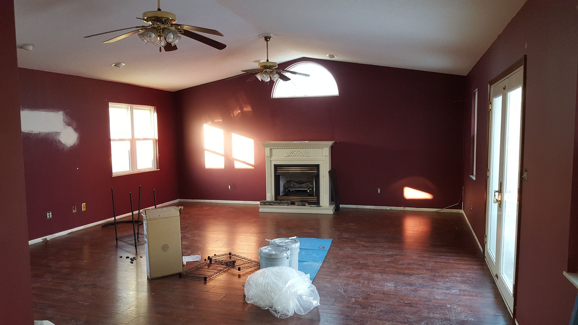Empty living room with burgundy walls, fireplace, two ceiling fans, and sunlight.