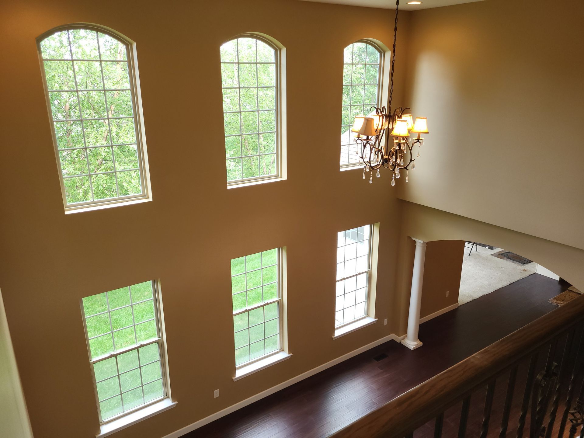 Interior view of a two-story foyer with arched windows, a chandelier, and dark hardwood floors.
