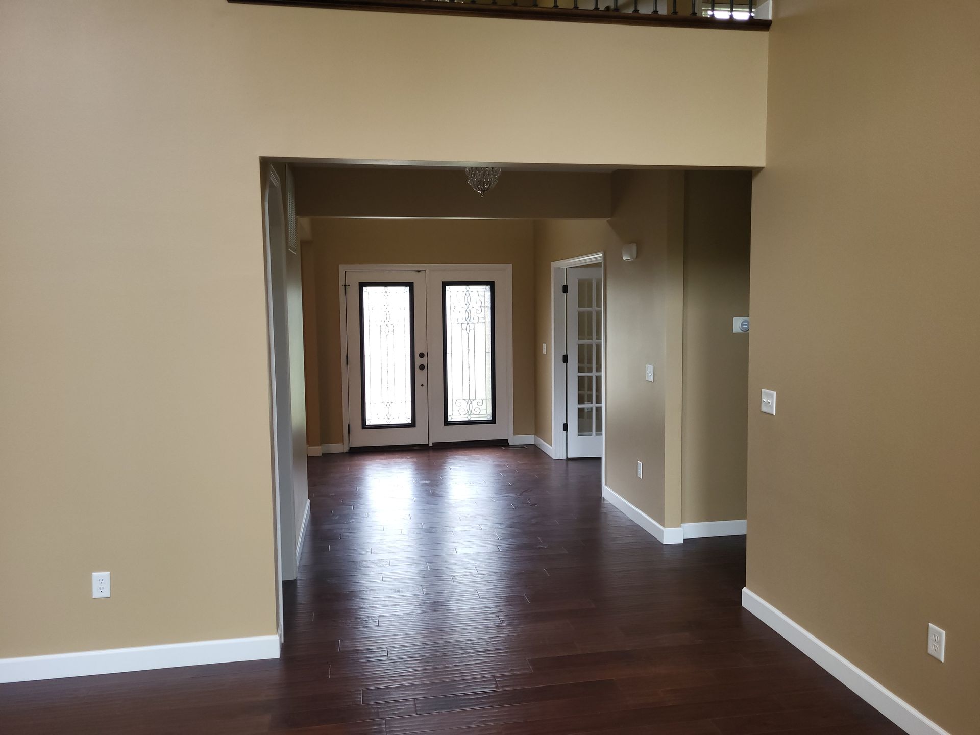 Interior view of a home entrance with double doors and a room with hardwood flooring. The walls are beige.