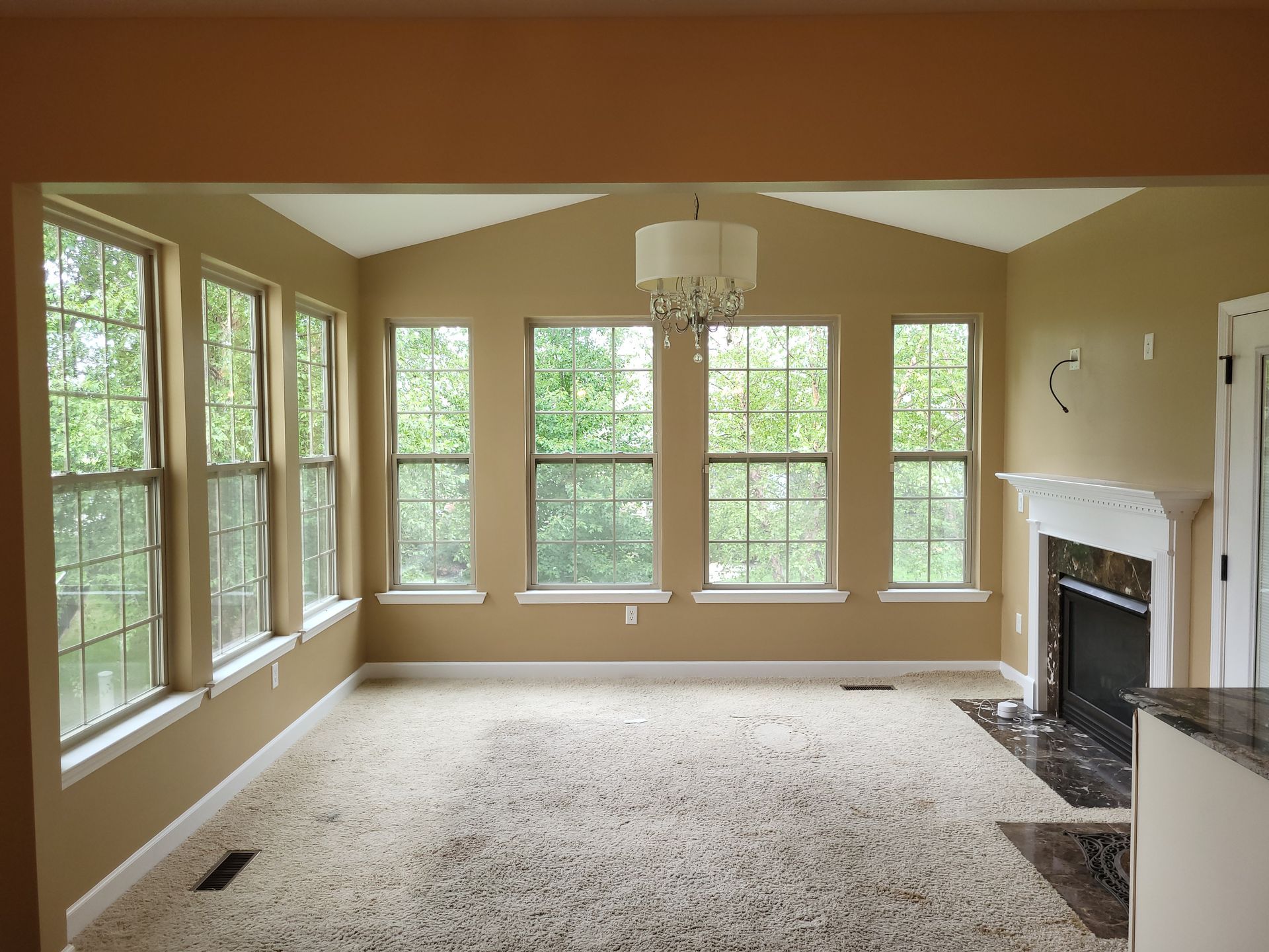 Sunroom with windows, neutral walls, carpet, fireplace, and chandelier.