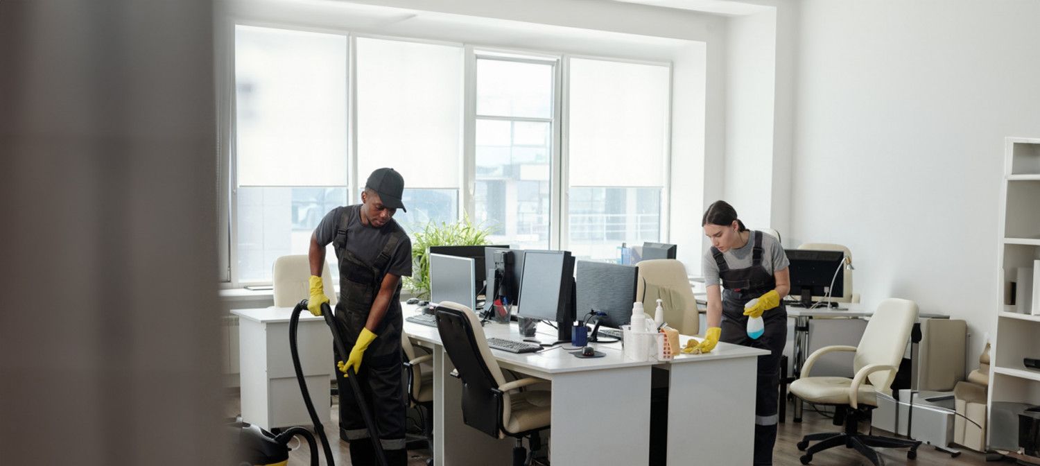 Office workers cleaning a bright modern workspace with desks, computers, and vacuum cleaners