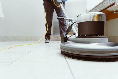 Person using a floor buffer on a white tile floor in a bright room