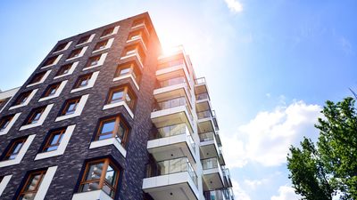 Sunlit brick apartment building viewed from below against a blue sky with trees
