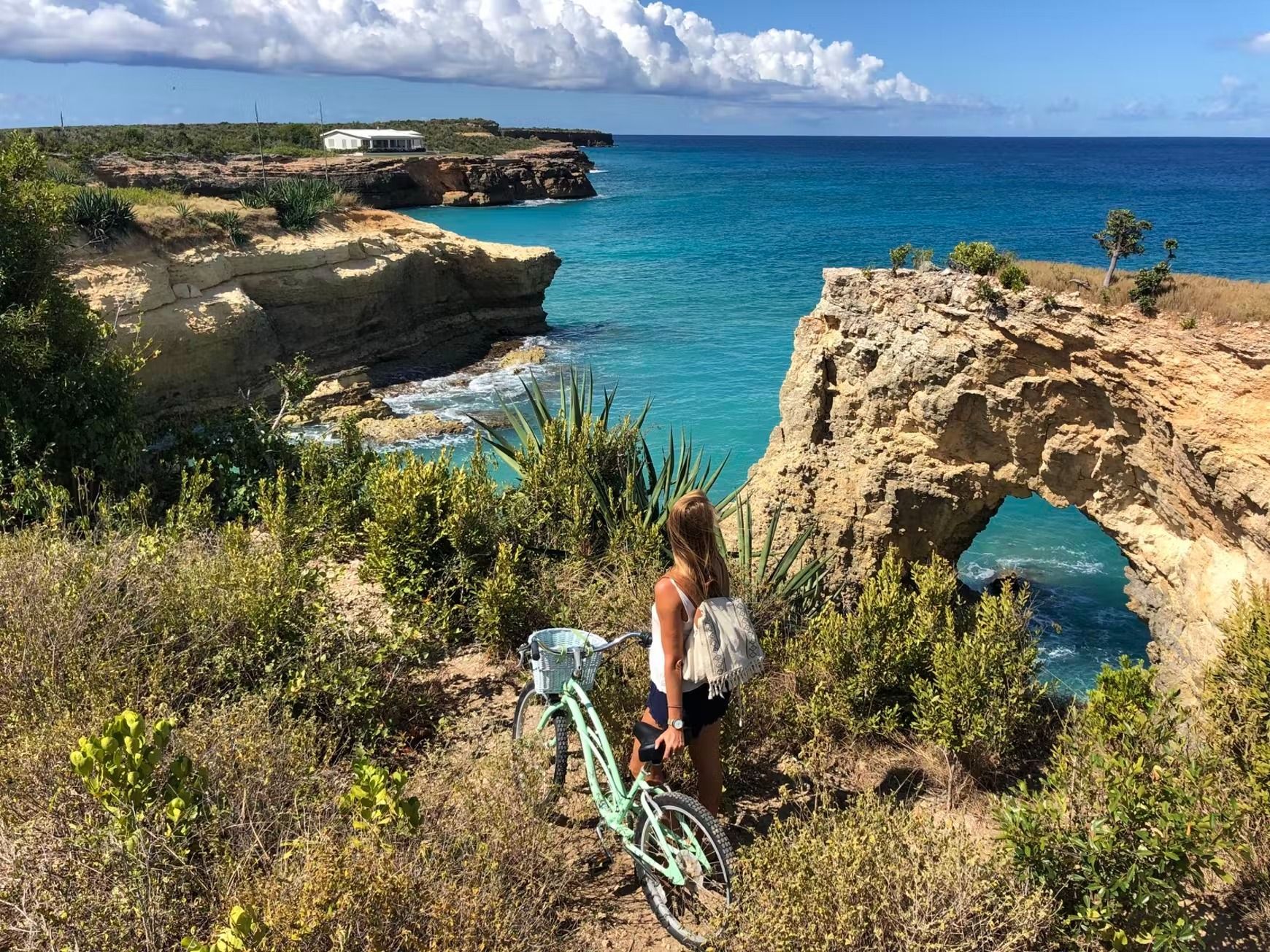 Woman looks at turquoise ocean from a rocky cliff with bike; natural arch.