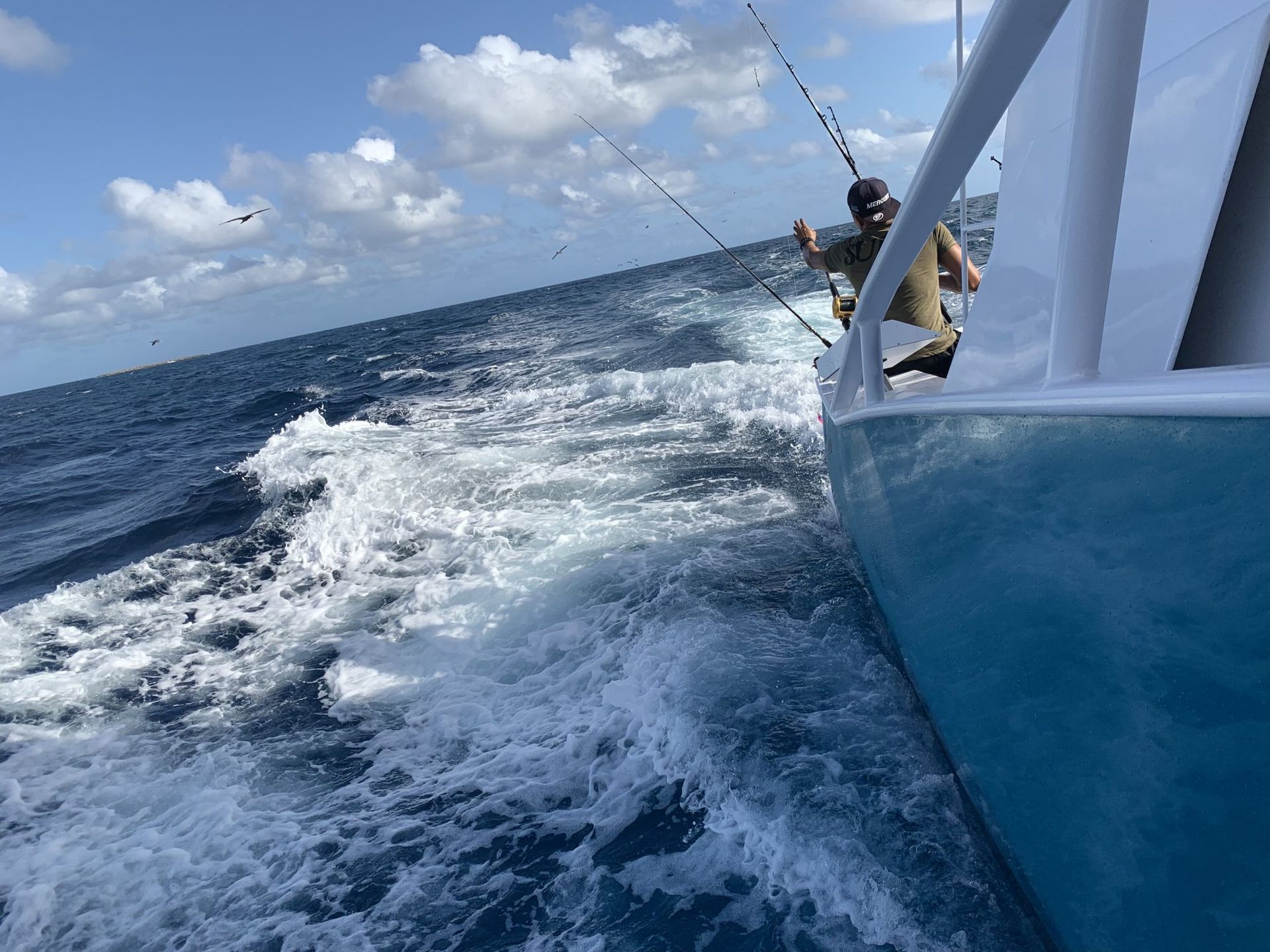Boat fishing on blue water with a person holding a fishing rod.