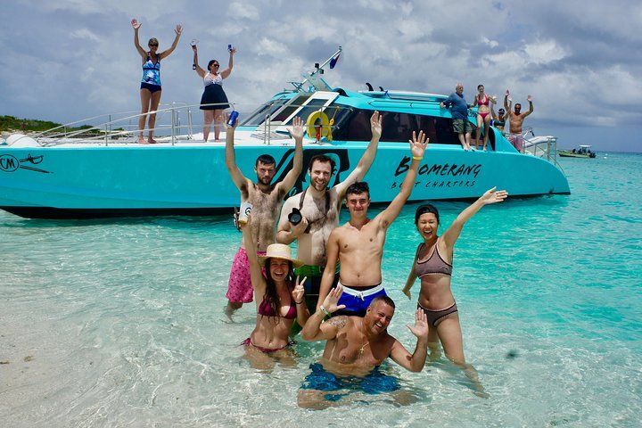 People celebrating in water near a turquoise catamaran boat. Sunny day.