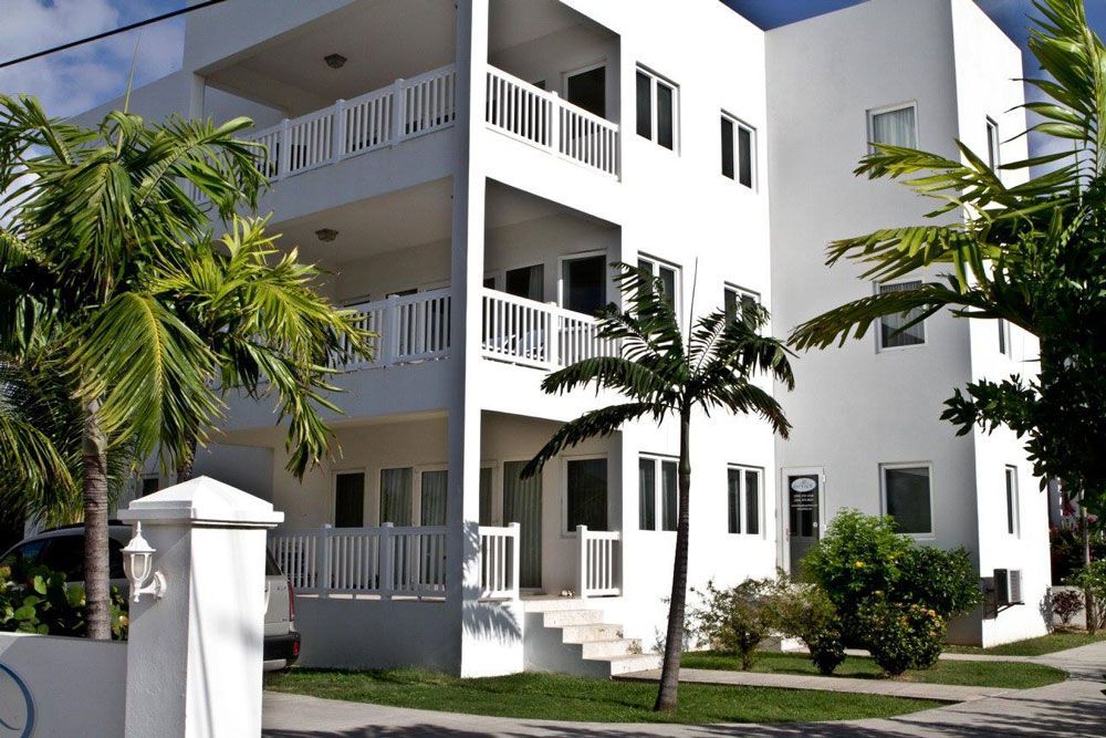 White multi-story apartment building with balconies, palm trees, and clear sky.