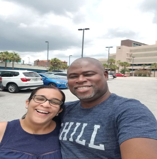 Smiling couple taking a selfie in a parking lot on a cloudy day.