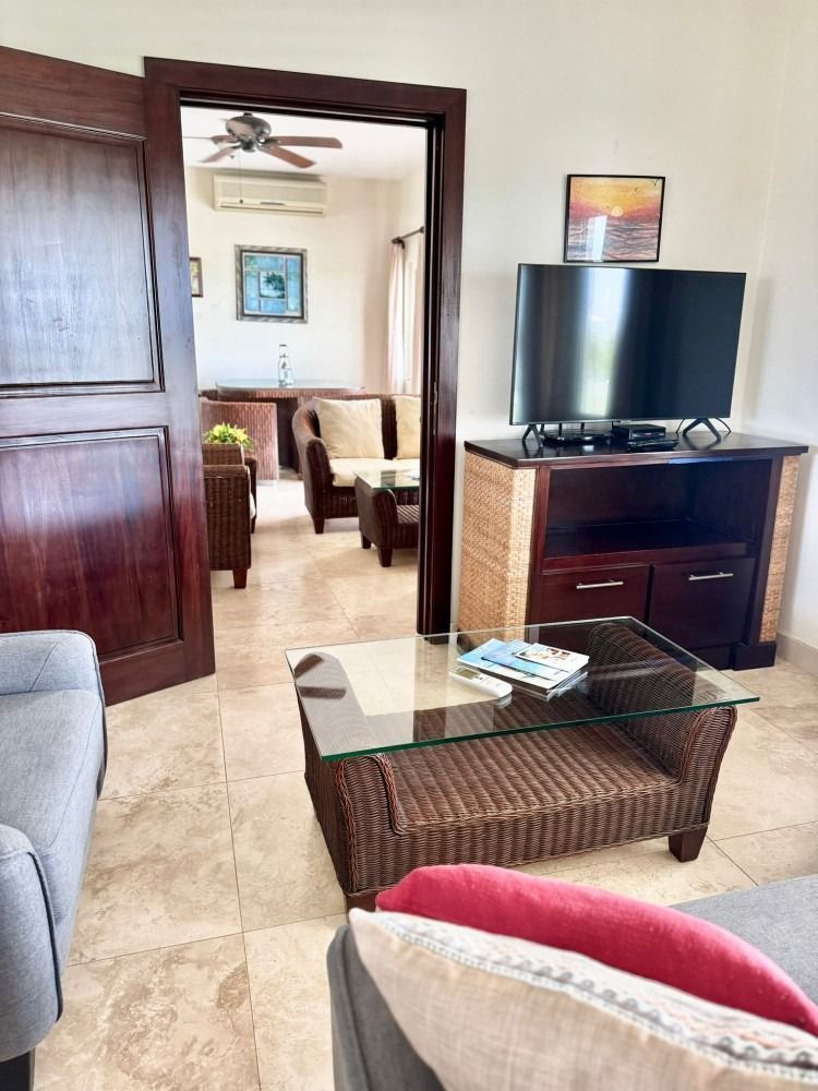 Living room with rattan furniture, TV, and open doorway to a sitting area. Beige tile floor.