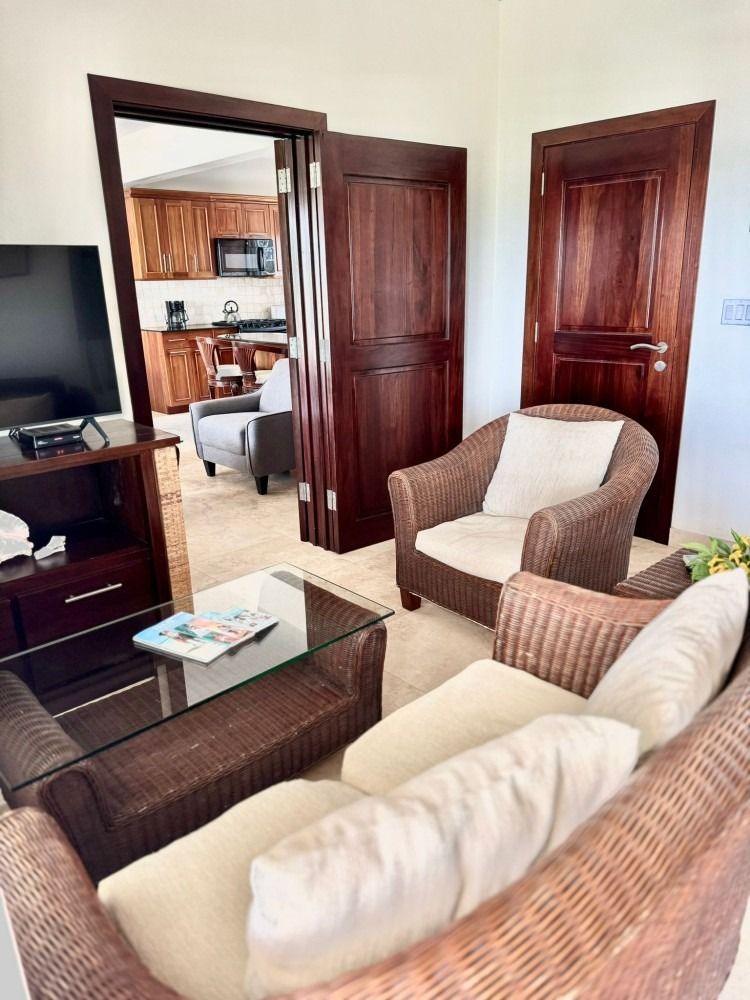 Living room with wicker furniture, a TV, and a view of the kitchen through an open doorway.