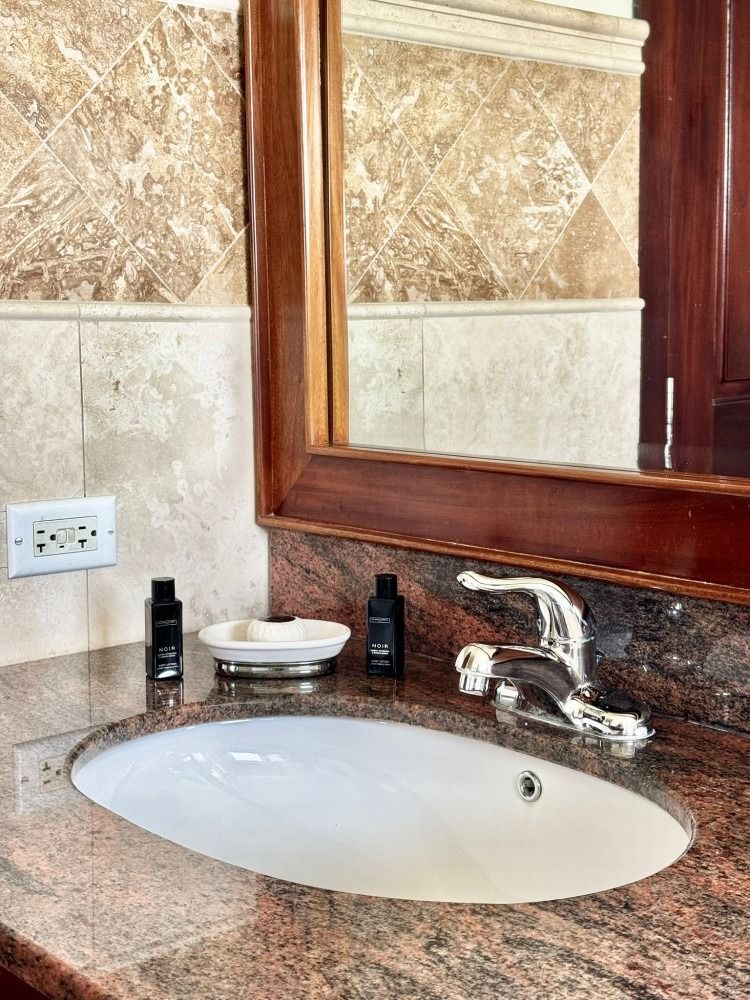 Bathroom sink with soap, toiletries, and a mirror on a granite countertop.