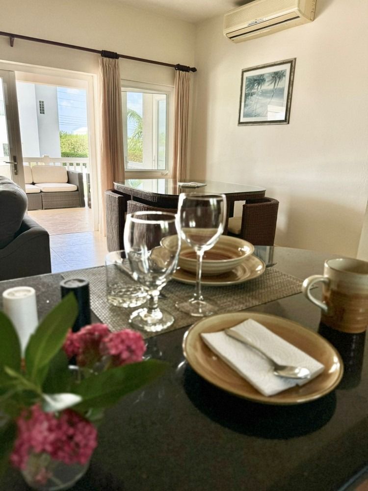 Dining table set for a meal, with an open door to a balcony. Two wine glasses and a flower arrangement.
