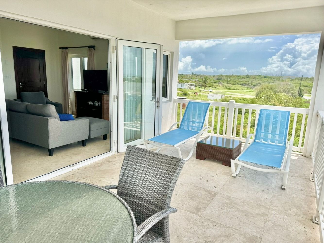 Balcony with two blue lounge chairs, small table, and a view of green landscape. Living room visible inside.