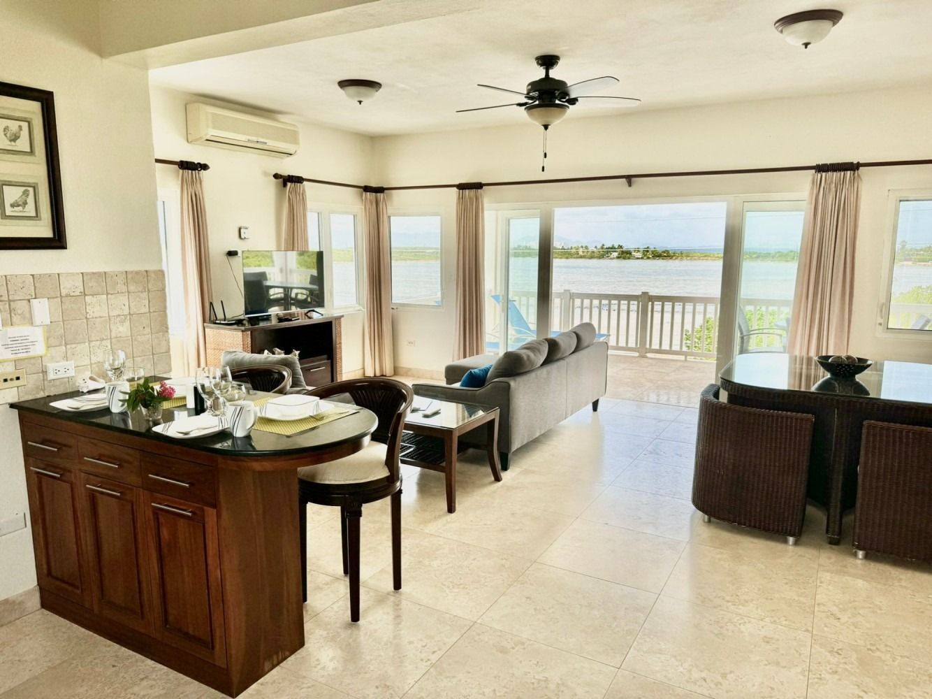 Bright open living room with kitchen island, ceiling fan, sofa, and balcony view of the water