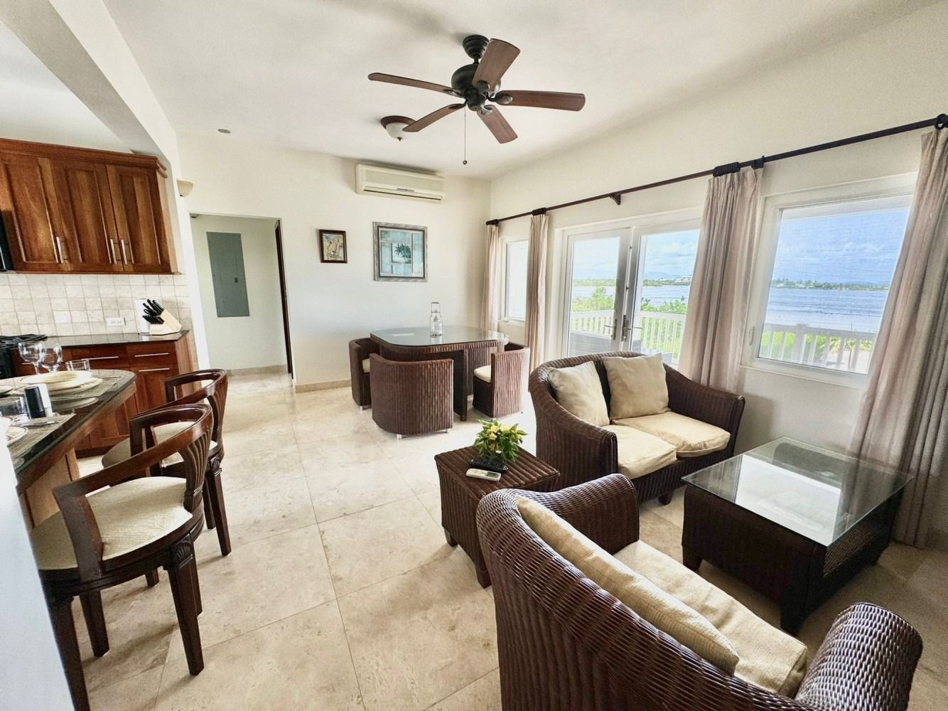 Bright living room with wicker chairs, sofa, ceiling fan, and large windows overlooking water.
