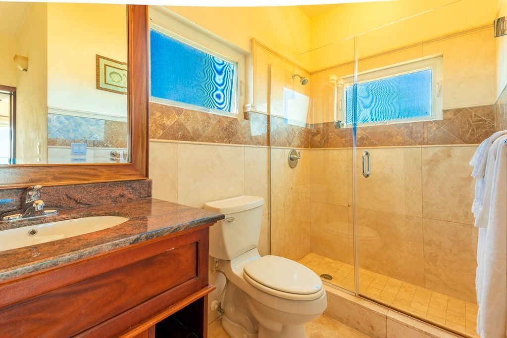Bathroom with wood vanity, marble countertop, glass shower, and patterned blue windows.