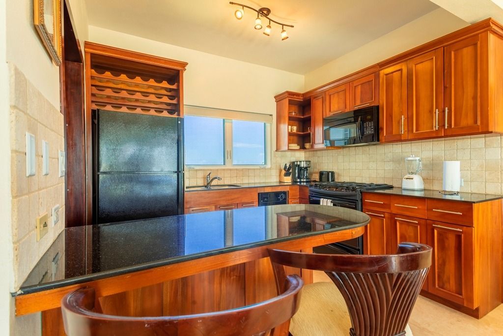 Kitchen with dark wood cabinets, black countertops, and a built-in bar.