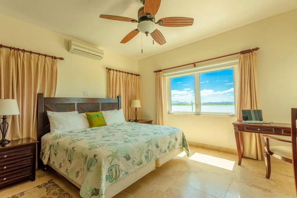 Bright bedroom with a bed, ceiling fan, windows, and desk in warm sunlight