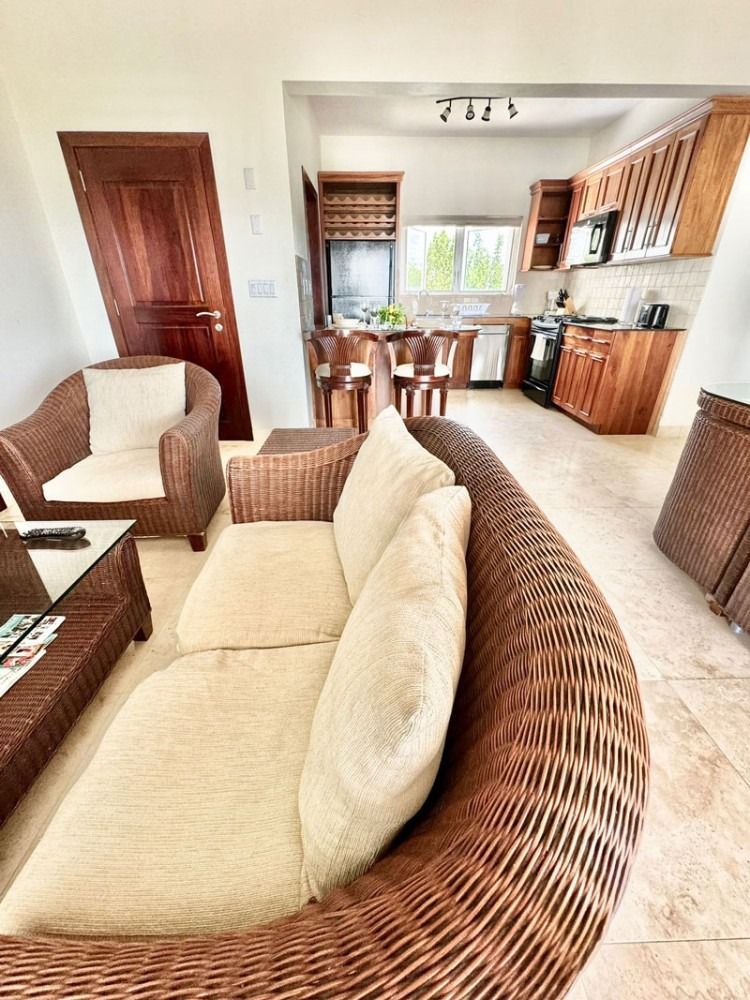 Living room with wicker furniture opening to a kitchen, featuring wooden cabinets and a breakfast bar.