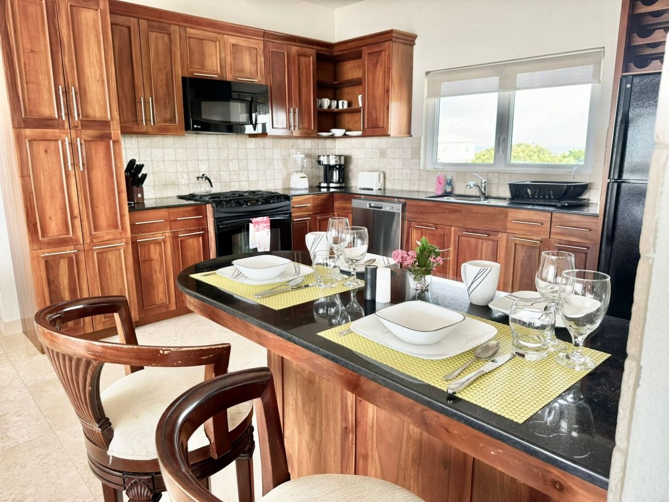 Kitchen with wooden cabinets, black countertops, and a breakfast bar set for two.