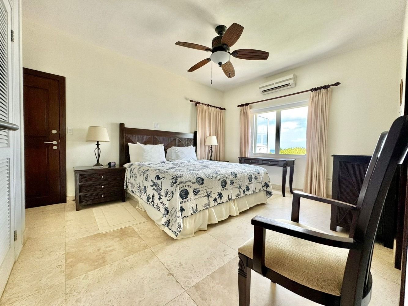 Bright bedroom with a bed, dresser, ceiling fan, window, and a chair on a tiled floor
